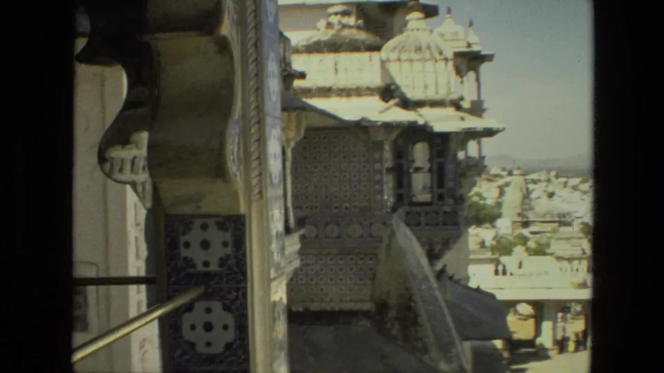 1974 India 8mm view of a tiled religious facade with a balcony-like opening and city buildings in the distance.