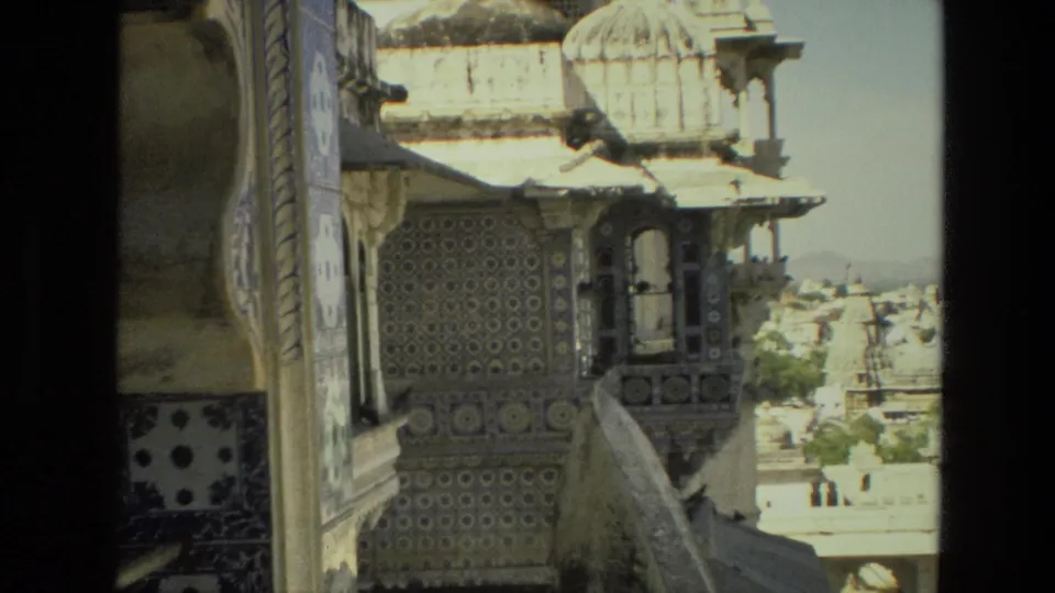 1974 India frame showing ornate patterned walls, a small arched balcony, domes, and the city beyond the monument.