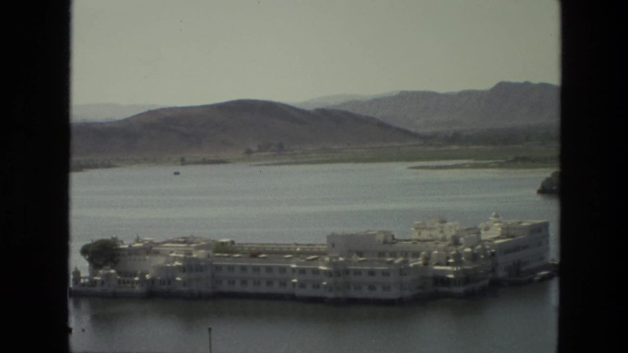 White island building complex on a calm lake with hills behind, seen through dark window borders.