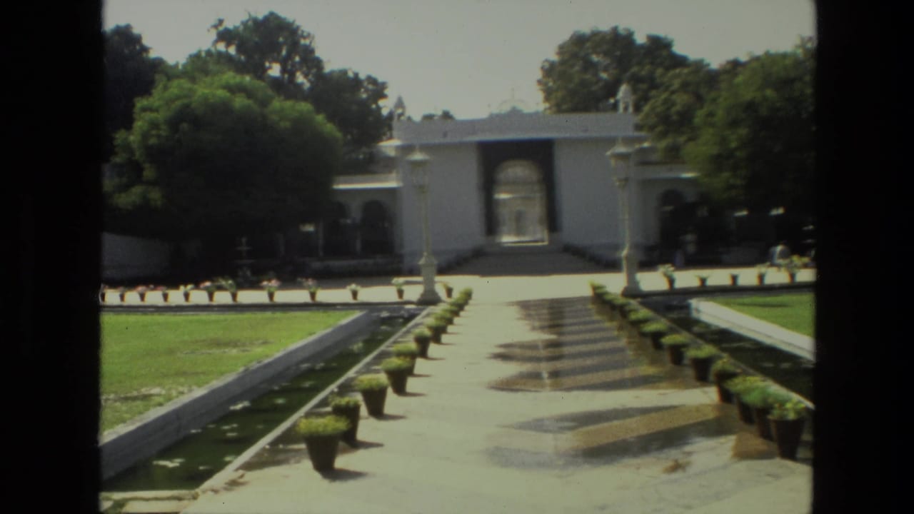 Formal garden path leading to a white arched gateway with lawns, potted plants, and narrow water channels.