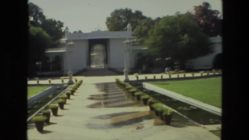 1974 India 8mm view of a formal garden with stone steps, white gateway, planters, lawn areas, trees, and a long shallow pool.