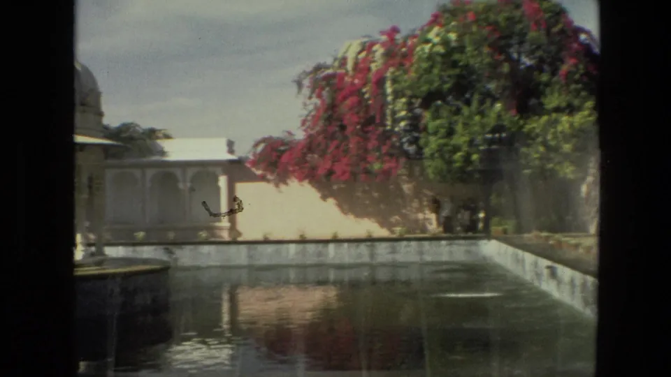 1974 8mm footage in India shows a courtyard pond, a distant figure, white arched structures, and bright bougainvillea above the wall.