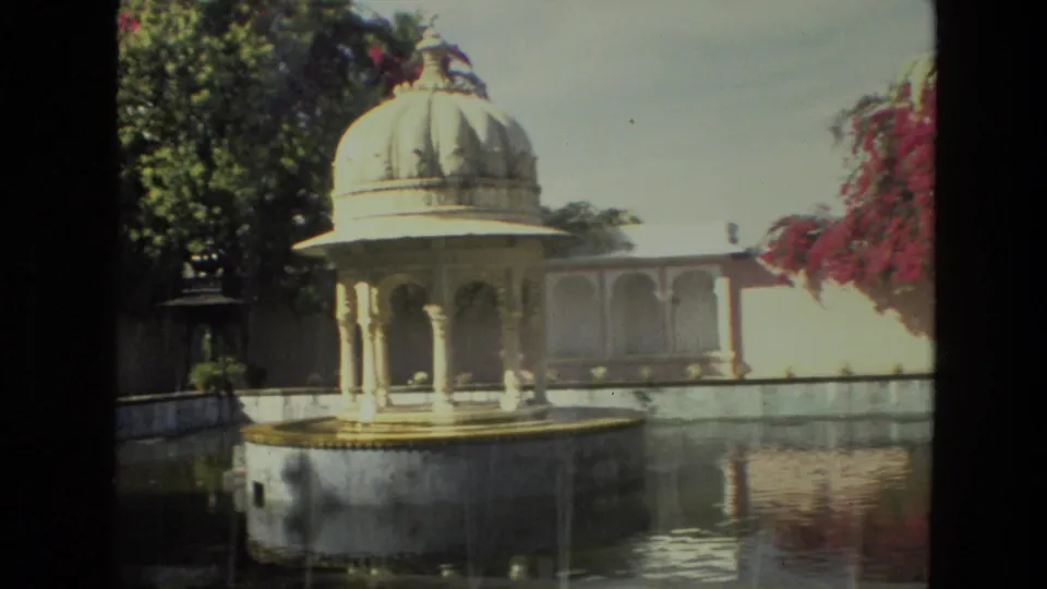 A domed pavilion rises beside the reflecting pond in this 1974 India courtyard view, with white arched buildings and bougainvillea in the background.