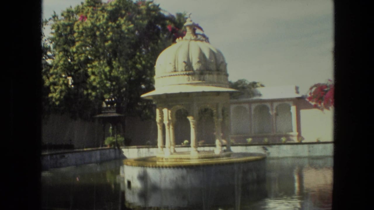 Domed fountain pavilion beside a still garden pool with trees and walls behind it.