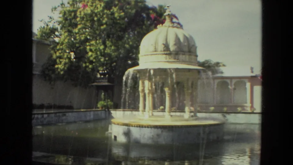 1974 8mm India footage showing water cascading from a domed pavilion fountain into a garden pool.