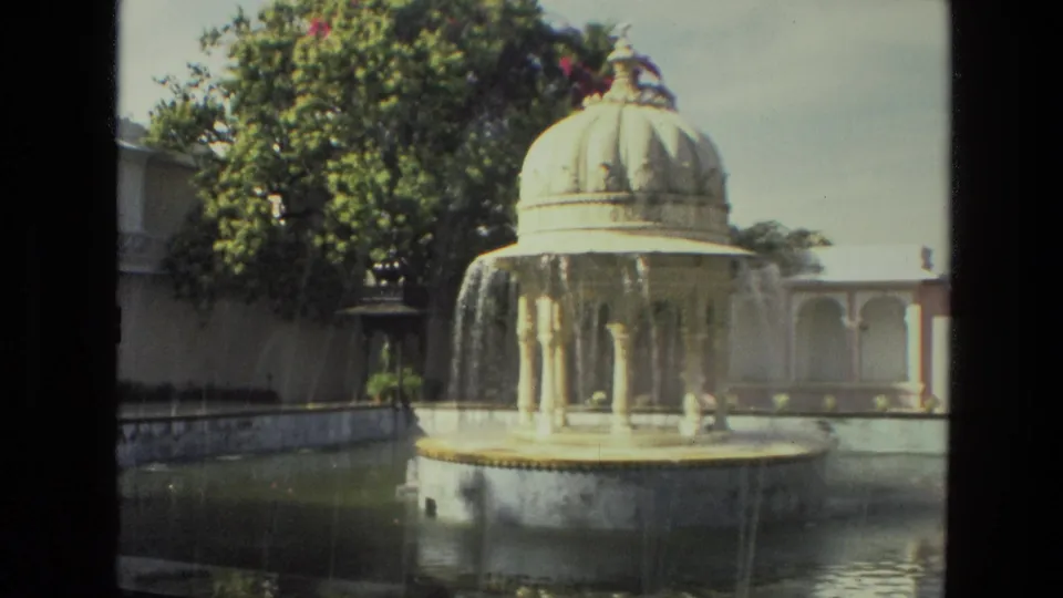 1974 8mm India footage showing the garden fountain running, with falling water, trees, walls, and a colonnade behind it.