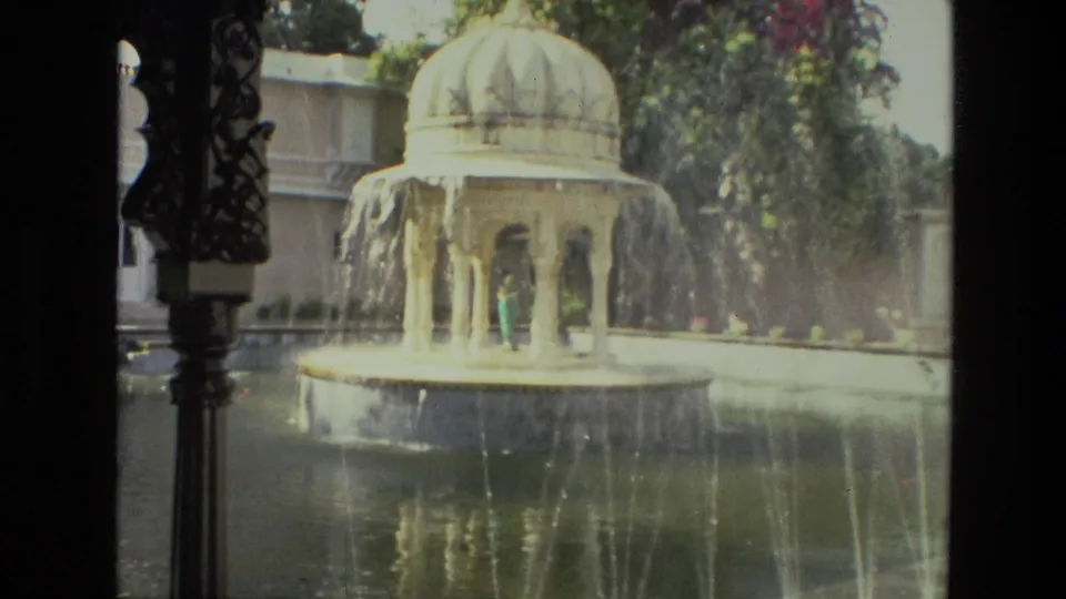 1974 8mm India footage showing a domed garden fountain spraying water, with a small indistinct visitor figure near the pavilion.