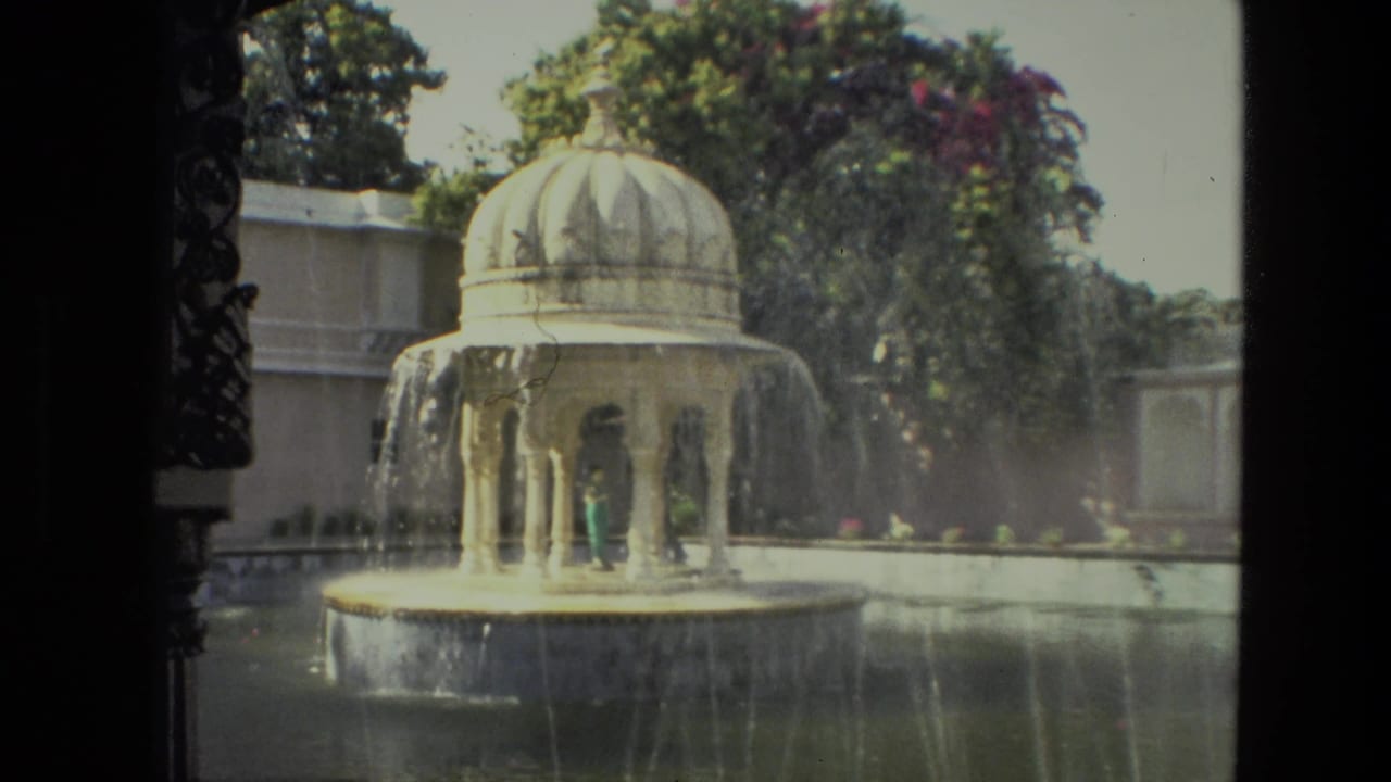 Domed garden fountain spraying water beside a pool and greenery.