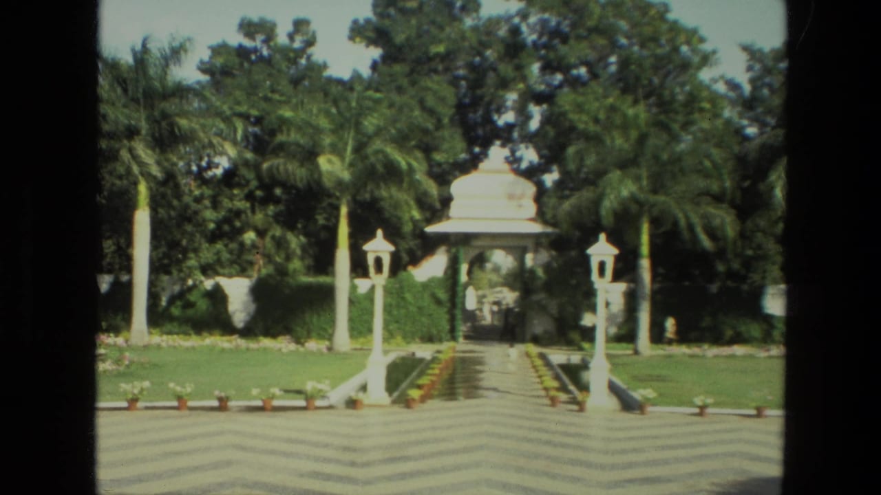 A formal Indian garden path leads between palm trees and white lamp posts toward a pavilion, captured on 1974 8mm film.