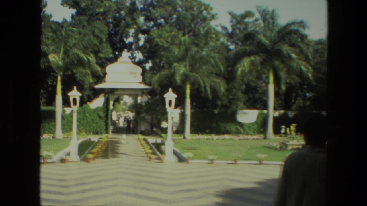 Wide courtyard path leading to a white domed garden gateway with palms and lamp posts.