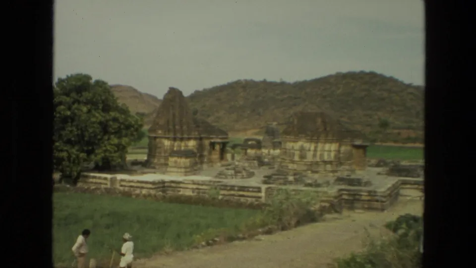 1974 India 8mm frame showing a temple complex below hills while two visitors walk along a path in the foreground.