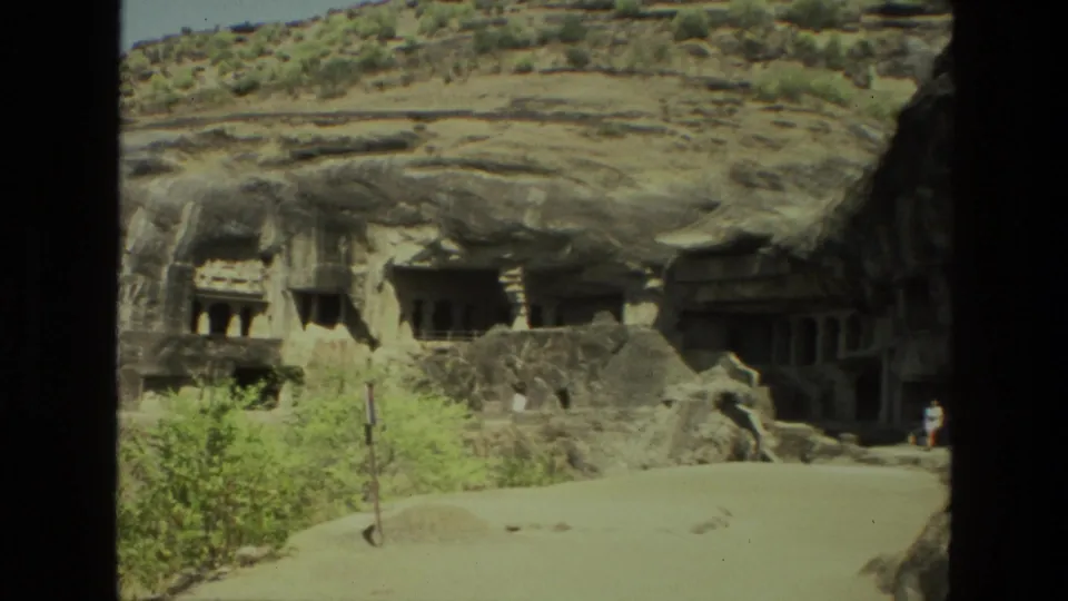 1974 India 8mm view of cave temple architecture in a rocky slope, with small visitors near the lower entrance.