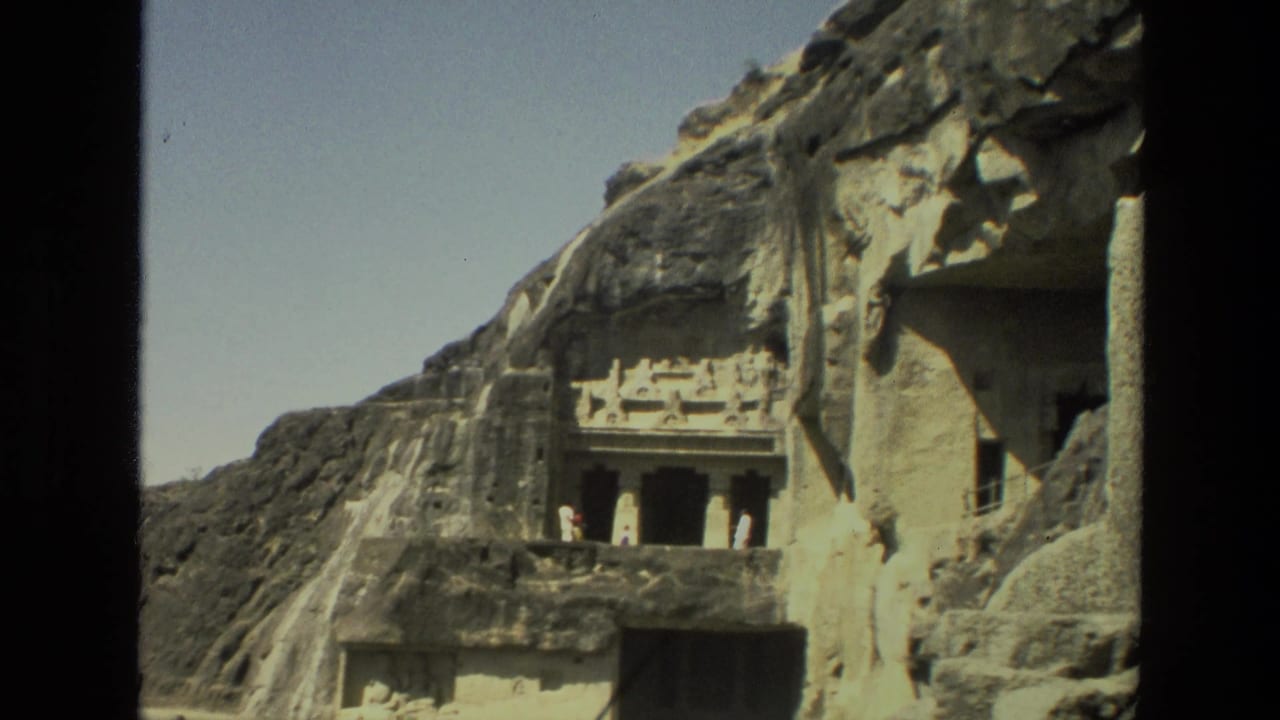 Carved cave temple entrance in a rock wall with visitors near the doorway.