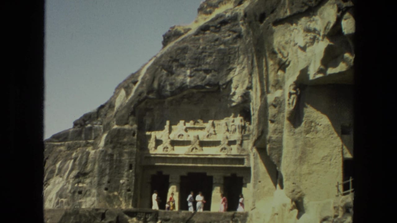 Visitors stand outside a carved rock-cut cave entrance below a cliff face.