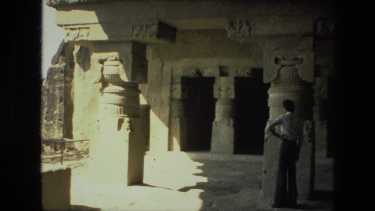 1974 India home-movie frame of a visitor looking across a stone ruin interior with carved pillars and deep shadowed entrances.