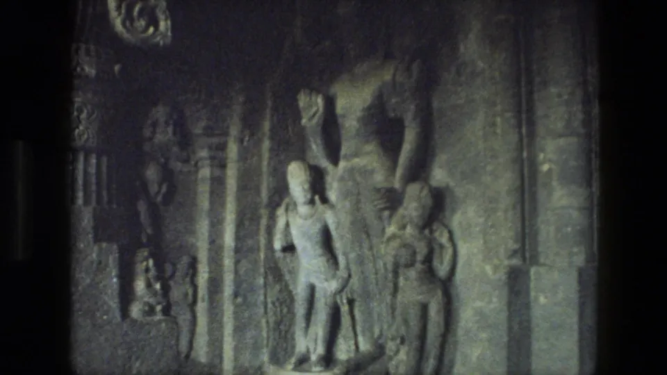 1974 India 8mm frame showing weathered carved figures and relief work on a dim stone wall inside the ruin.