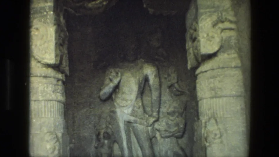 Visitor-shot 8mm view of an Indian temple relief showing a carved figure in a shadowed stone recess.