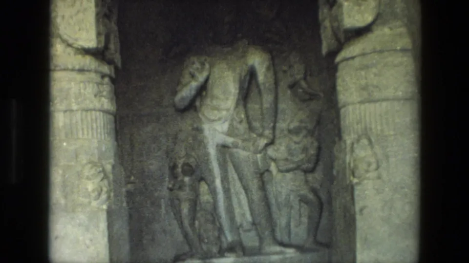 1974 8mm India travel frame showing weathered carved figures in a stone relief, framed by column-like architectural edges.
