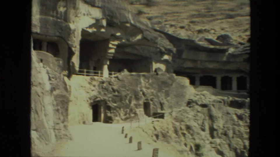 1974 India 8mm frame showing a closer visitor view of cave temple entrances cut into rugged stone.