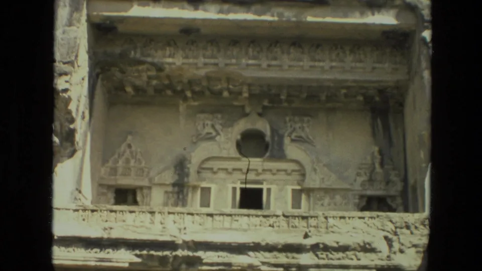 1974 India 8mm frame of an ornate rock-cut temple facade with carved relief details and a central arched opening.