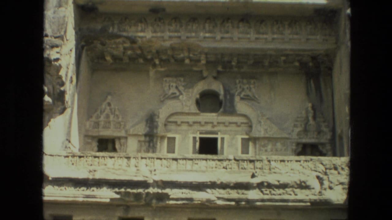 Carved stone building facade with ornate upper details and dark openings.