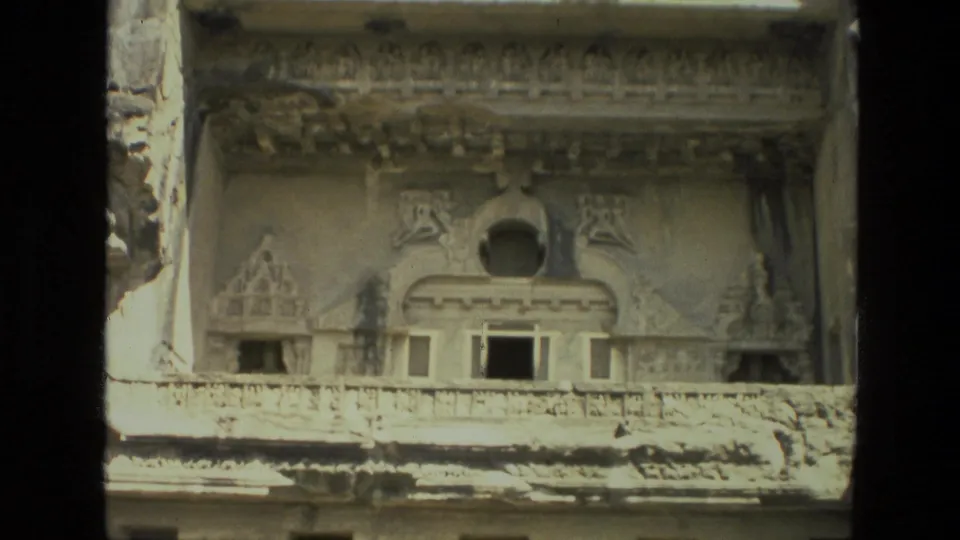 1974 8mm India travel frame showing a weathered carved stone facade with decorative upper forms and rectangular openings.