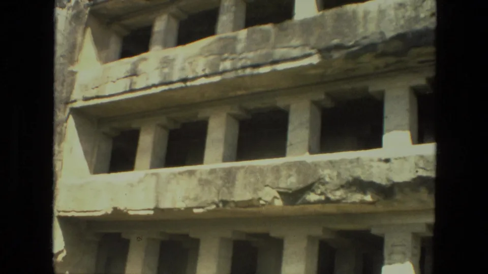 1974 8mm India frame showing the lower tier of a carved stone monument with columns and shadowed openings.