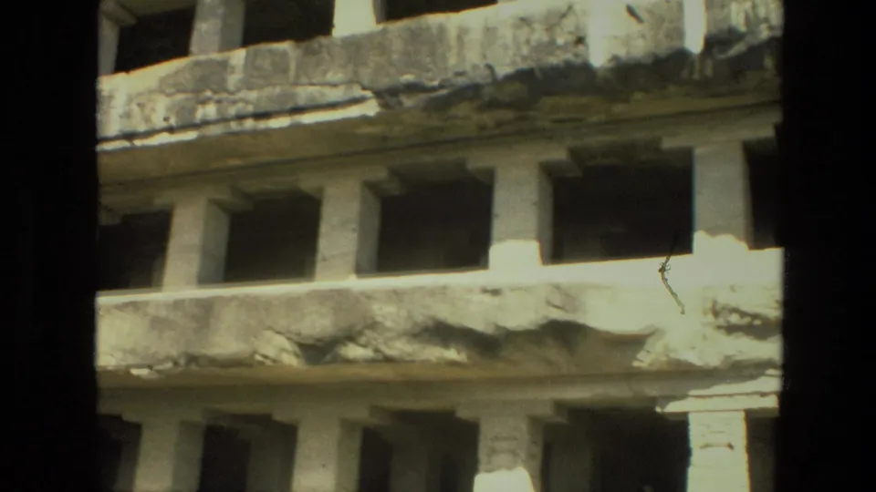 1974 India 8mm frame of a sunlit carved stone level with columns, rough ledges, and deep shadowed recesses.