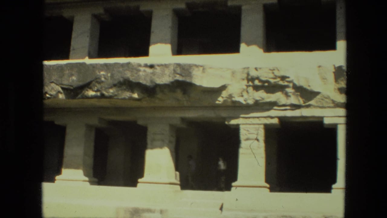 1974 India home-movie frame of a worn stone structure, with column supports below a damaged ledge and dark recessed rooms.
