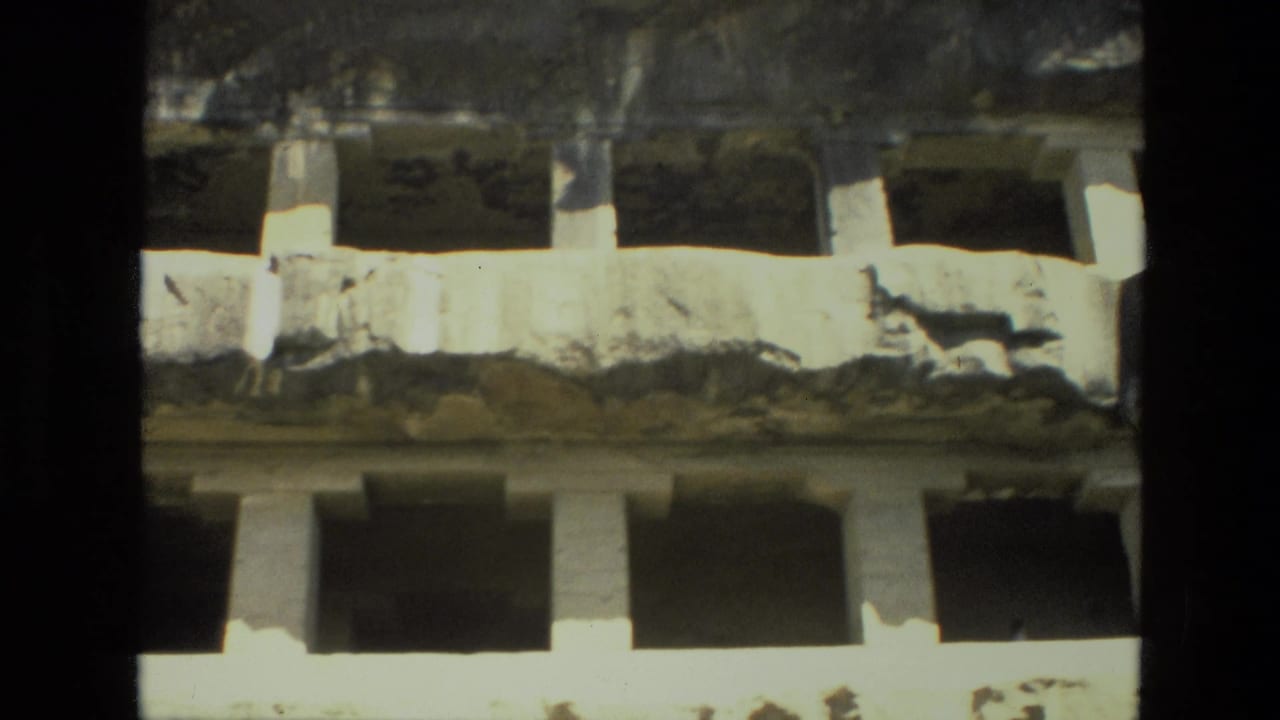 Weathered stone facade with rectangular openings and damaged carved surfaces.
