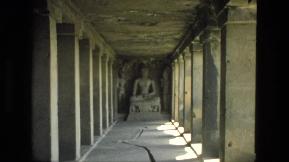 1974 India 8mm frame of a weathered temple passage with rectangular sunlight patches and a seated religious figure at the end.
