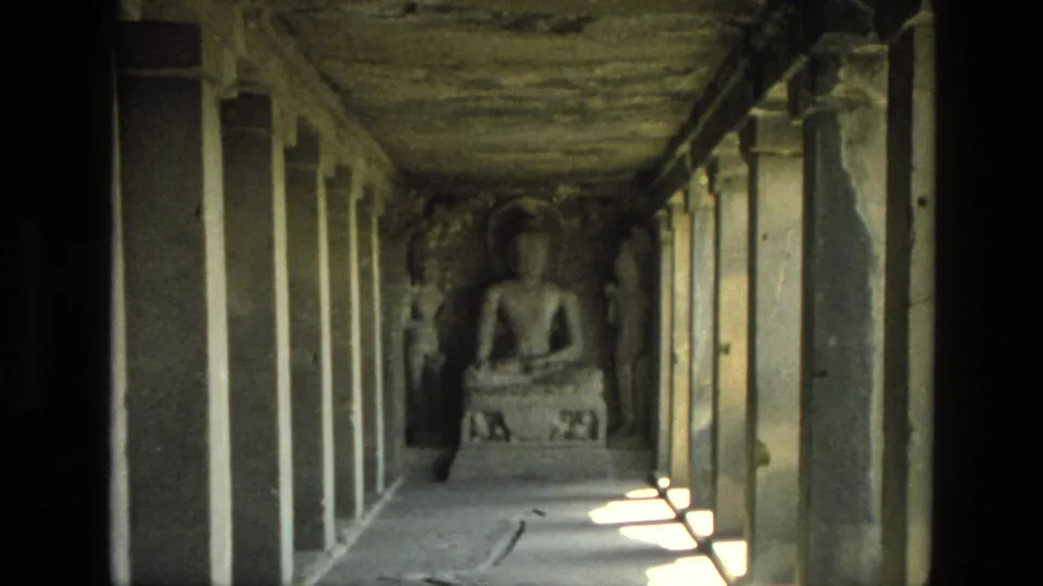 1974 India 8mm frame showing a closer visitor view of a seated religious statue framed by worn pillars and side carvings.