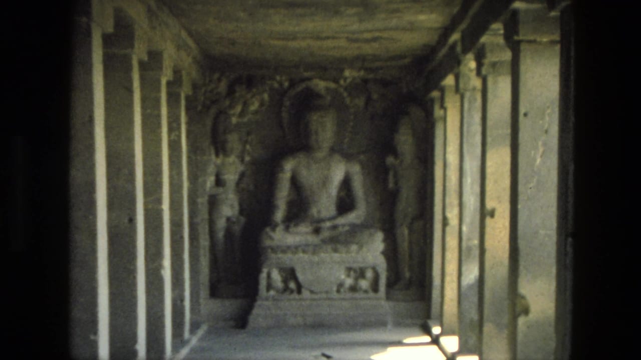 Seated Buddha statue inside a shadowed stone corridor with carved figures and pillars.