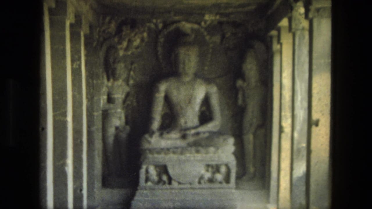 1974 India 8mm frame with a seated Buddha sculpture inside a carved cave-temple chamber, flanked by pillars and relief figures.
