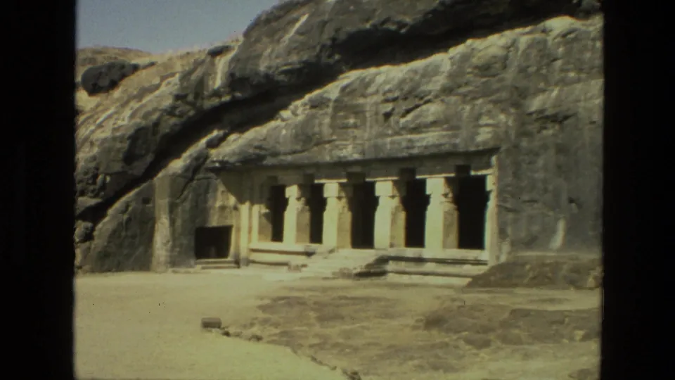 1974 India 8mm frame showing an exterior rock-cut temple facade with stone columns carved into a cliff face.