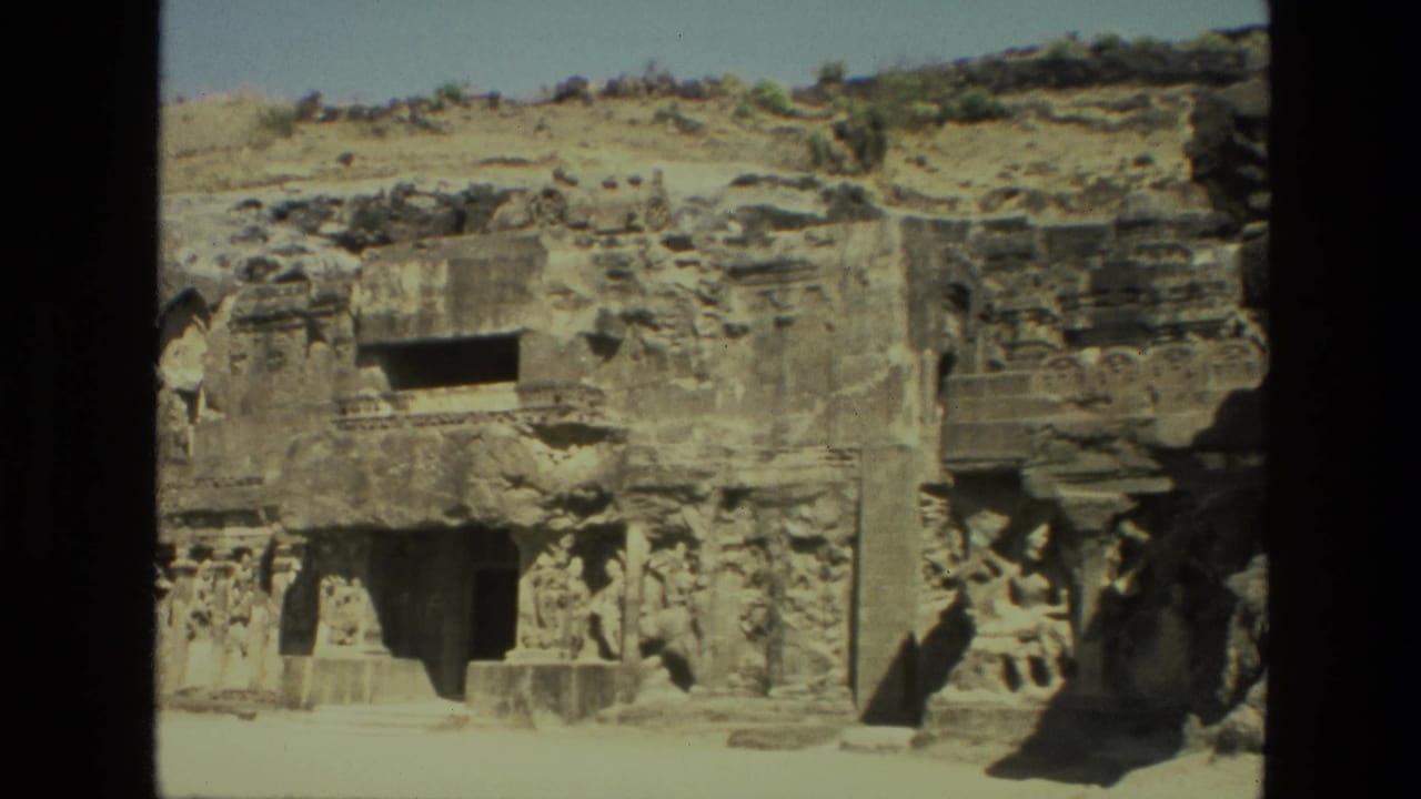 1974 India 8mm frame showing an Ellora Caves rock-cut facade with carved columns, hillside stone, and shadowed openings.