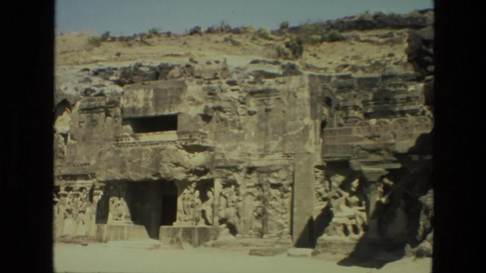 1974 India 8mm frame showing an Ellora Caves rock-cut facade with carved columns, hillside stone, and shadowed openings.