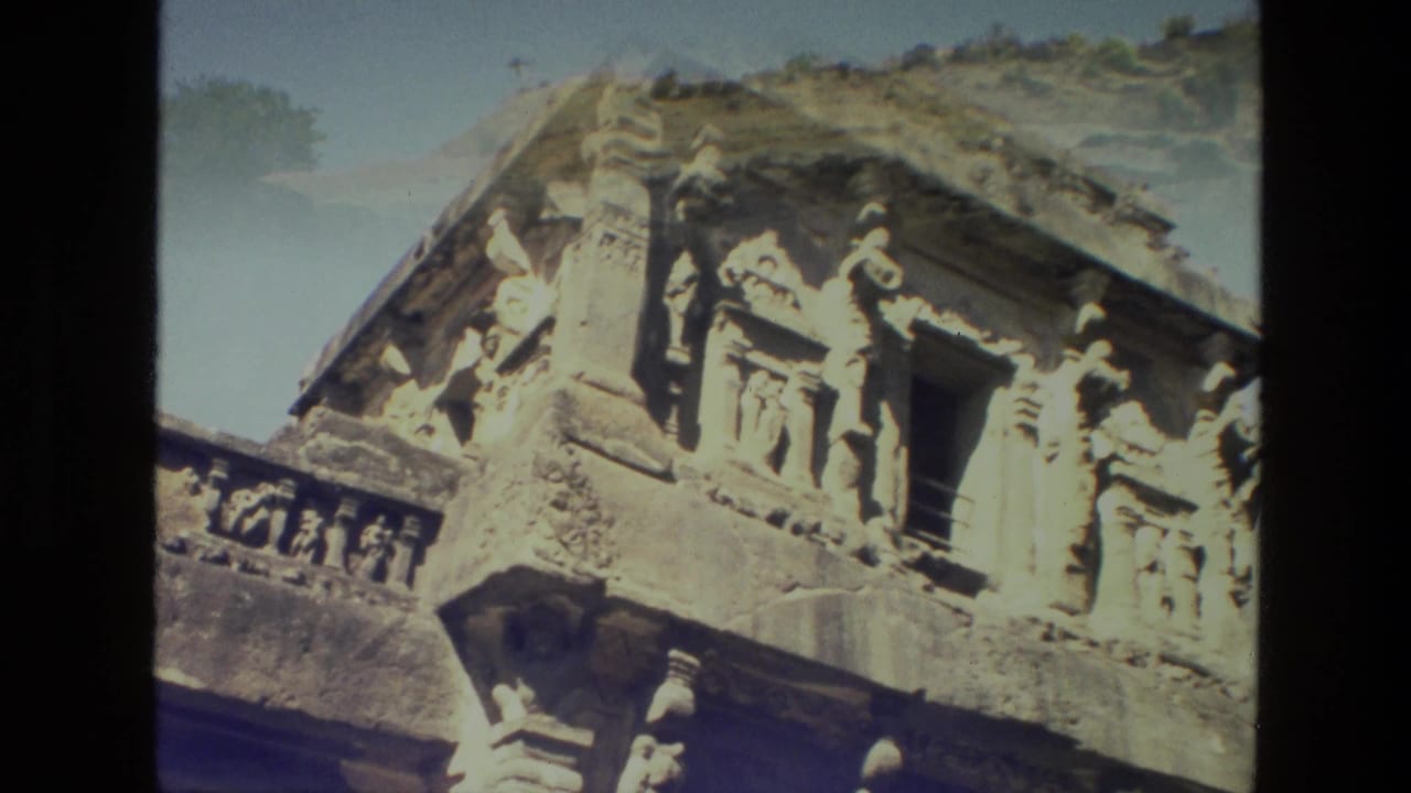 Close 1974 India travel-film view of carved Ajanta stone figures and architectural details around a dark doorway.