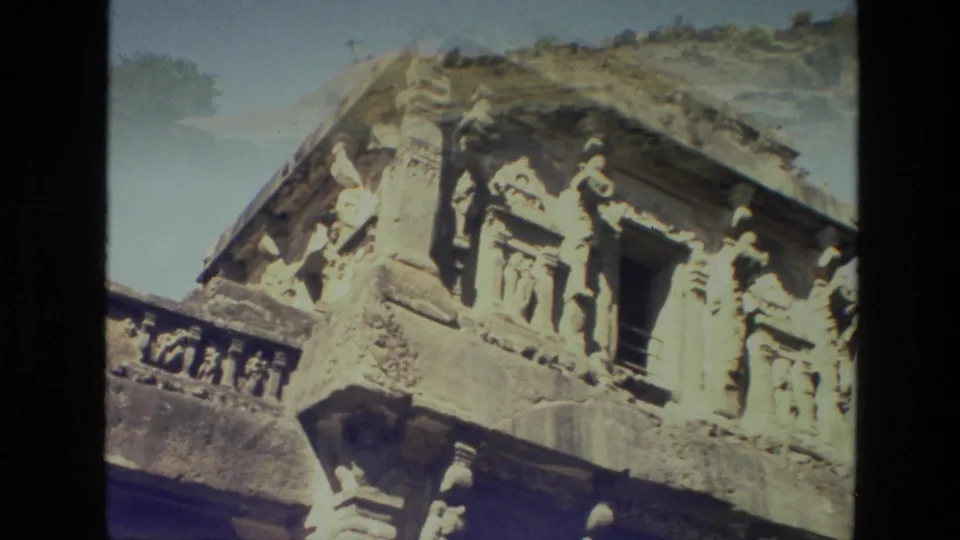 Close 1974 India travel-film view of carved Ajanta stone figures and architectural details around a dark doorway.