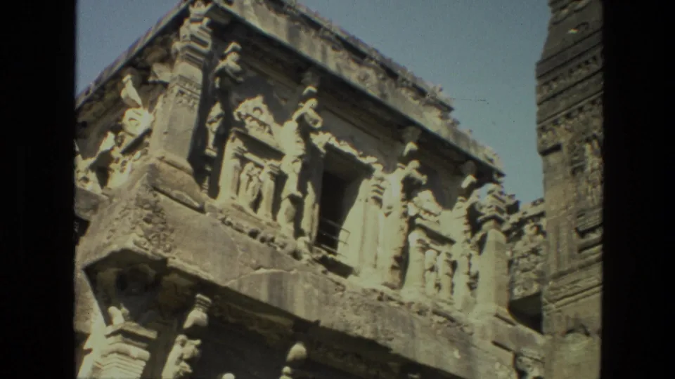 Angled 8mm close-up of Ajanta Cave carvings in India, showing sculpted figures, a dark doorway, and weathered stone detail.