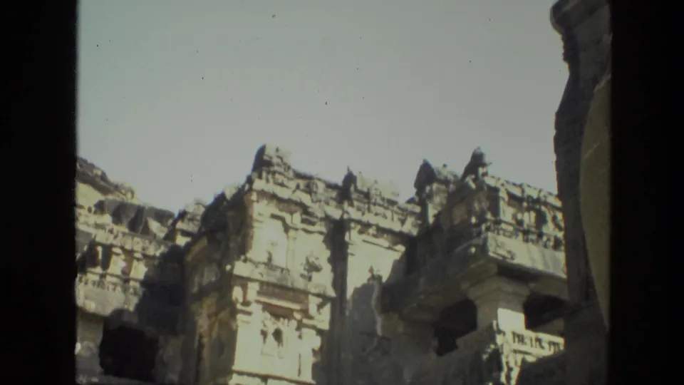 1974 8mm India footage showing a carved stone facade and dark openings in a cliffside ruin under strong sunlight.