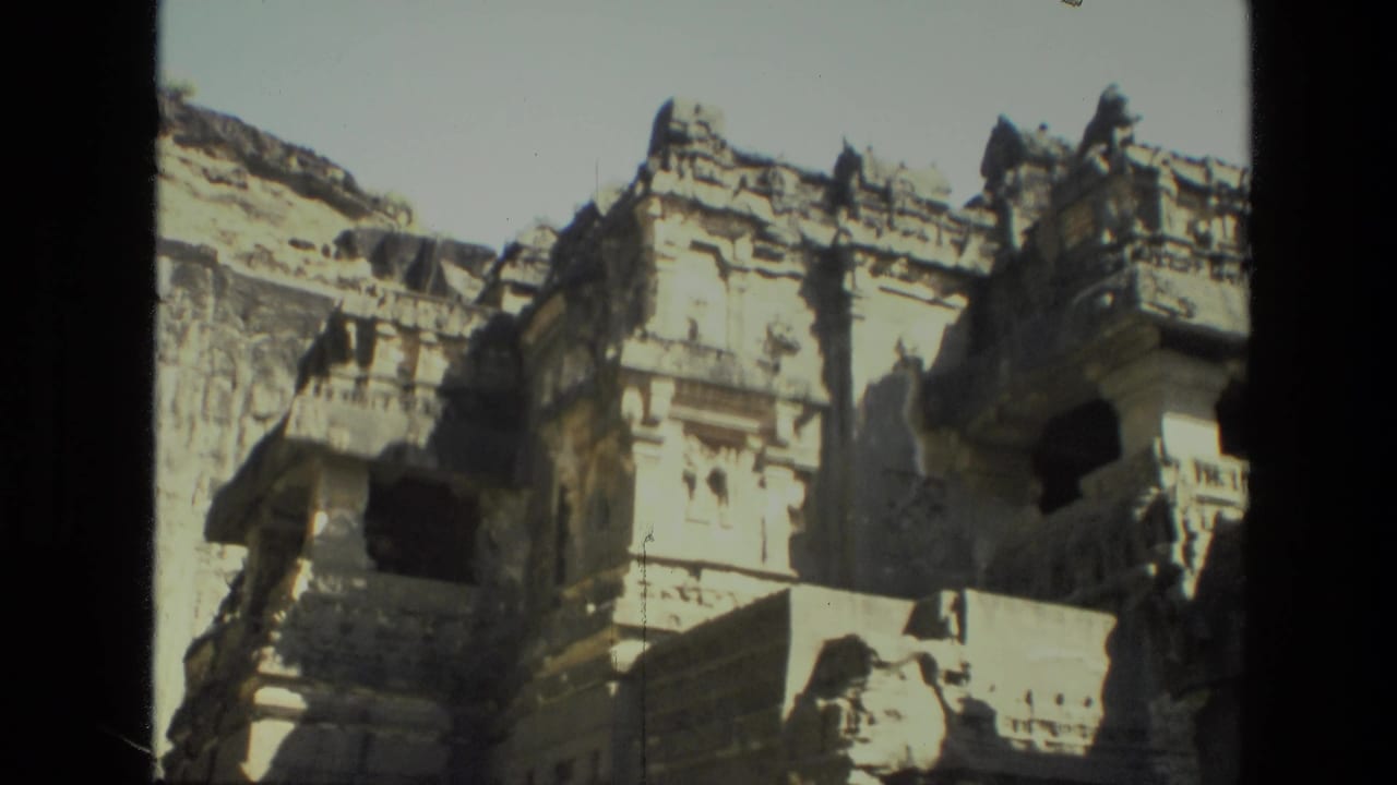 A visitor-shot view of Indian rock-cut architecture, with weathered carved details and deep shadowed window-like openings.
