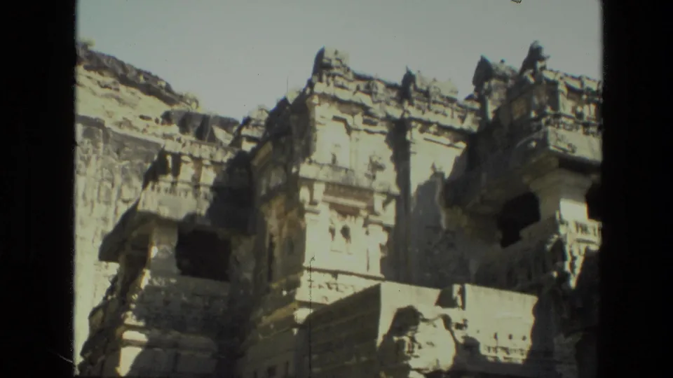 A visitor-shot view of Indian rock-cut architecture, with weathered carved details and deep shadowed window-like openings.
