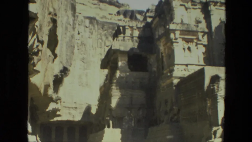 Final frame shows sunlit rock-cut architecture in India, with a rough cliff wall, carved columns or ledges, and deep shadows.