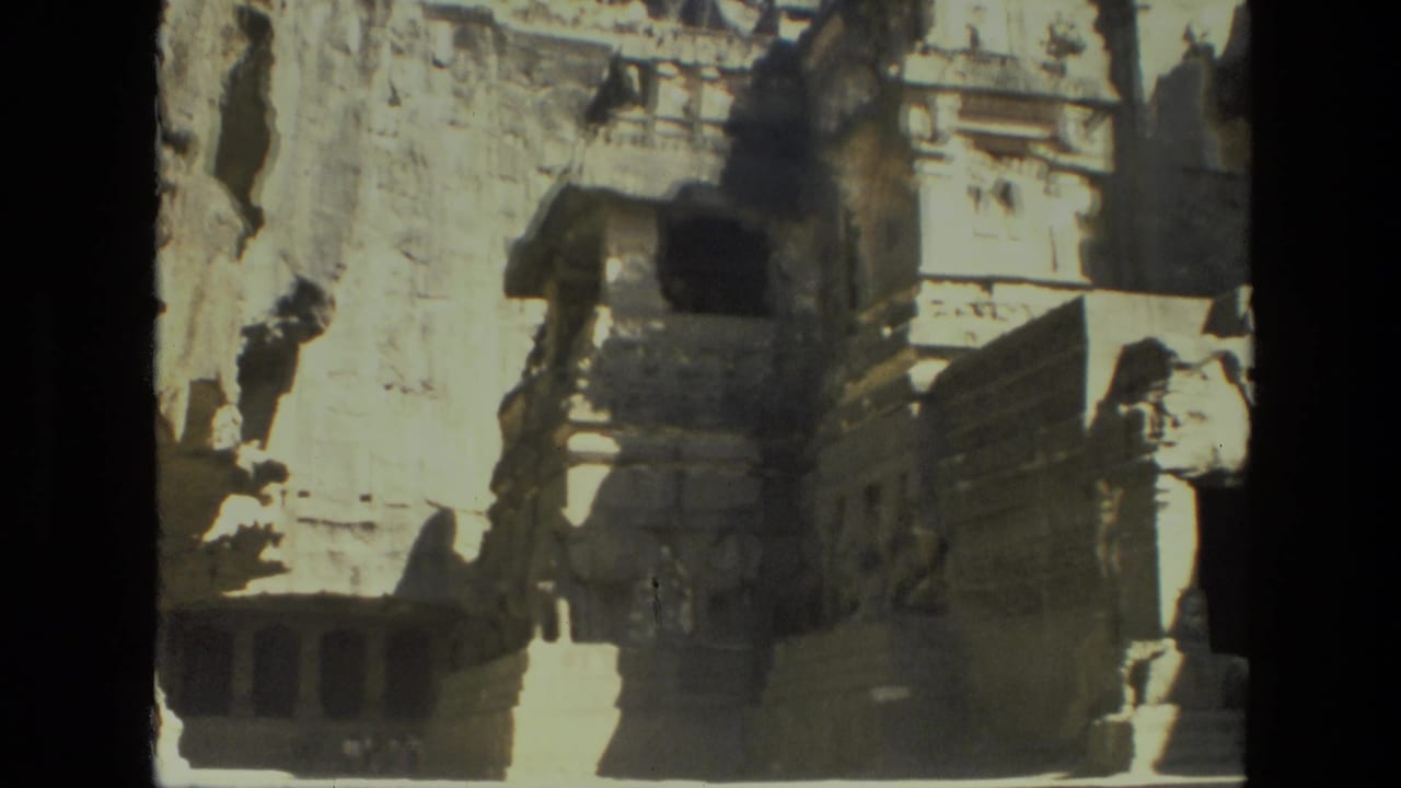Cliff-carved stone temple facade with stairs and weathered architectural details in bright sun.