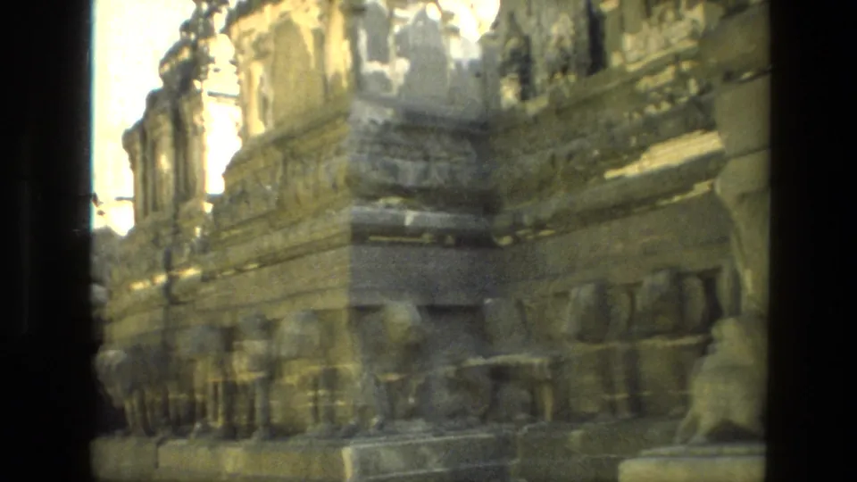 1974 India frame showing weathered stone architecture with carved base details, ledges, and strong sunlit highlights.