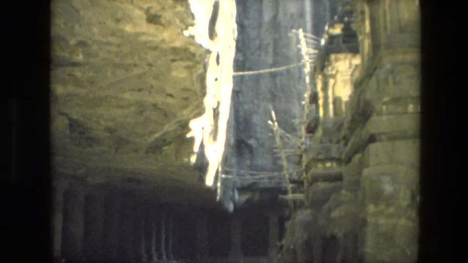 1974 India 8mm frame of a shadowed carved stone interior with columns, railings, scaffolding, and strong light spill.
