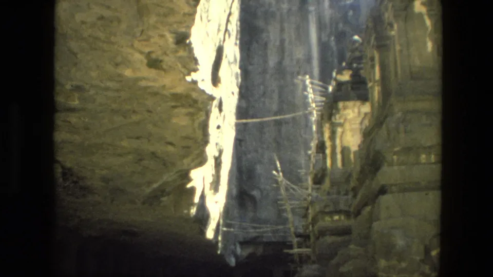 1974 India 8mm view of a rock-cut architectural area with scaffolding, railings, and a dark opening in the stone.
