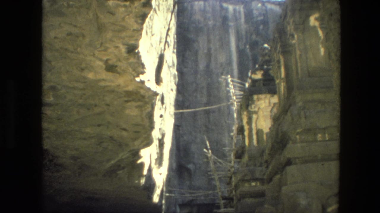 Rock-cut opening with sunlit stone walls and a shadowed temple structure beyond.
