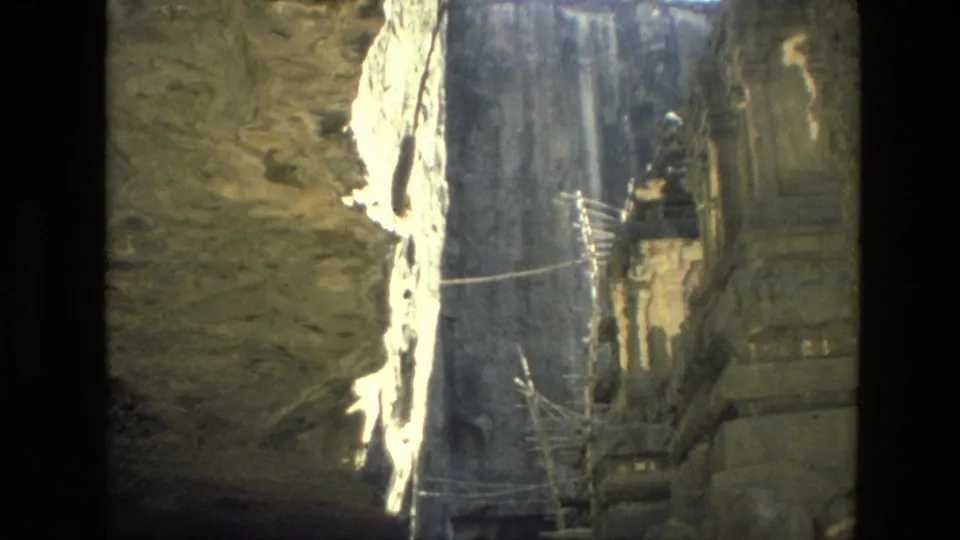 1974 India 8mm frame showing a rock-cut passage, bright stone face, and shadowed carved temple architecture beyond.